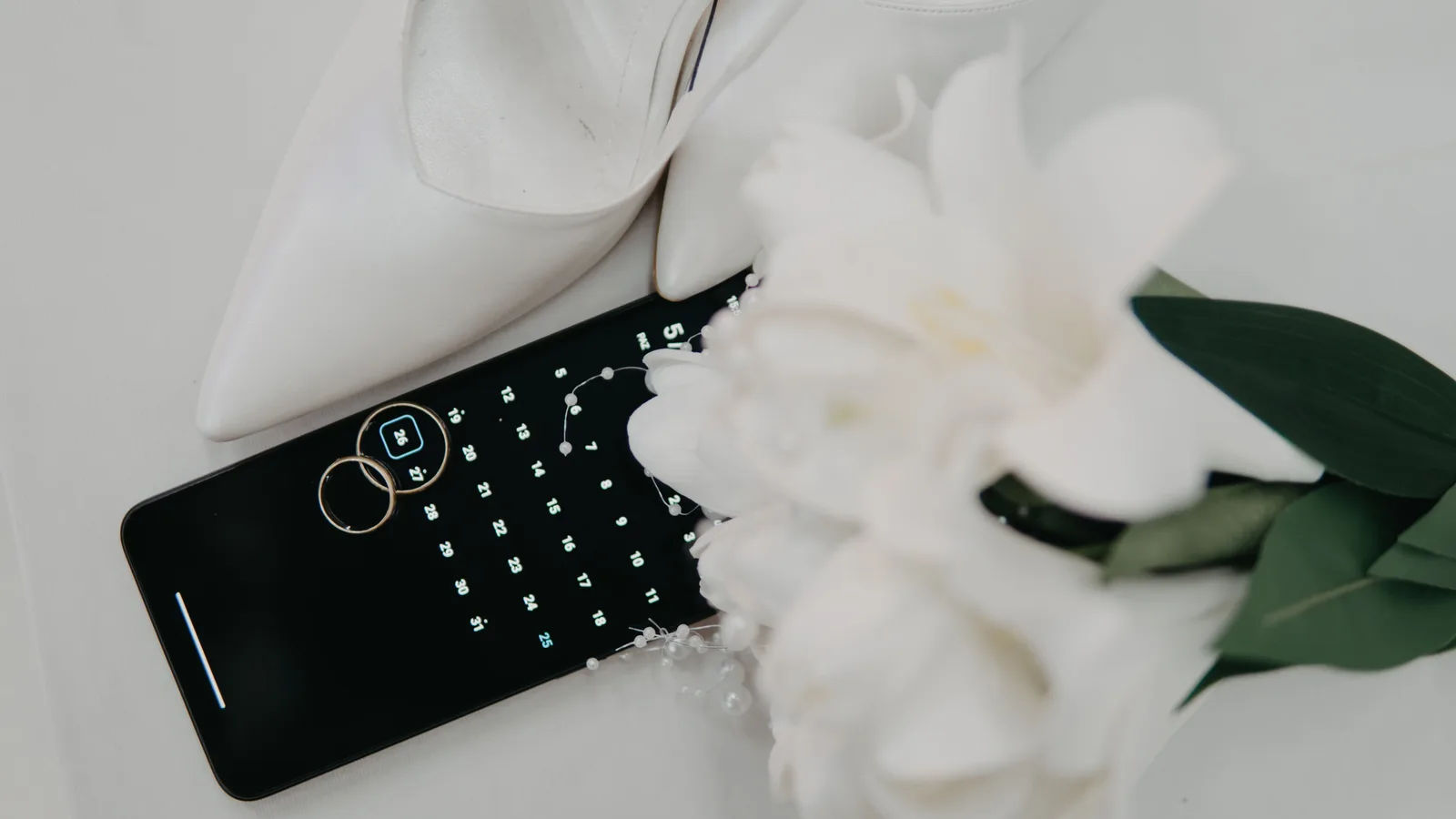 Flat lay of wedding essentials including high heels, rings, and a bouquet on a calendar. Reading wedding planning bookkeeping with a sceptical eye